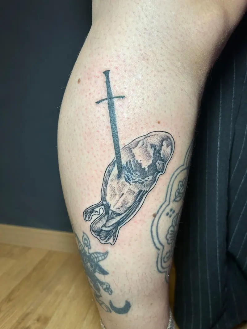 Blackwork-Tattoo eines von einem Schwert durchbohrten Vogels am Unterschenkel, gestochen von Cindy