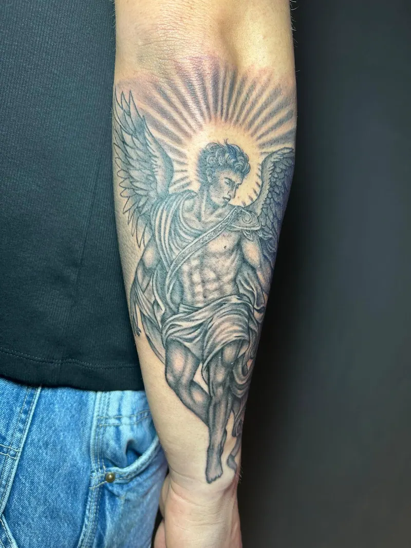 Black-&-Grey-Tattoo eines Engels mit Flügeln vor einem Strahlenkranz am Unterarm, gestochen von Cindy