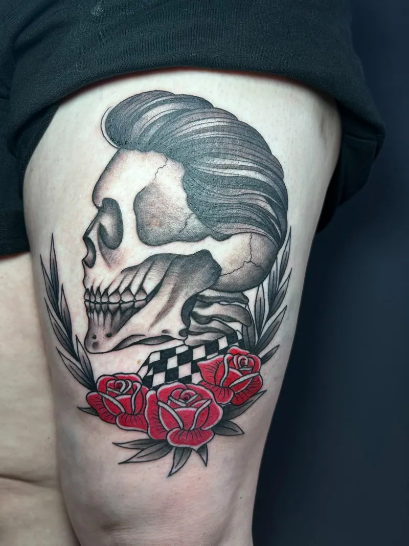 Tattoo eines Totenkopfs mit Haartolle, Schachbrettmuster und roten Rosen am Oberschenkel, gestochen von Cindy