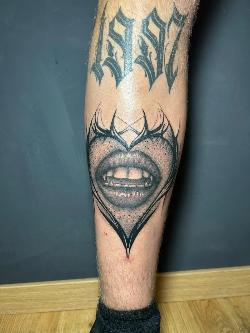 Black-&-Grey-Tattoo von Lippen mit Vampirzähnen in einem Herz, darüber die Jahreszahl „1992“, am Unterschenkel, gestochen von Cindy
