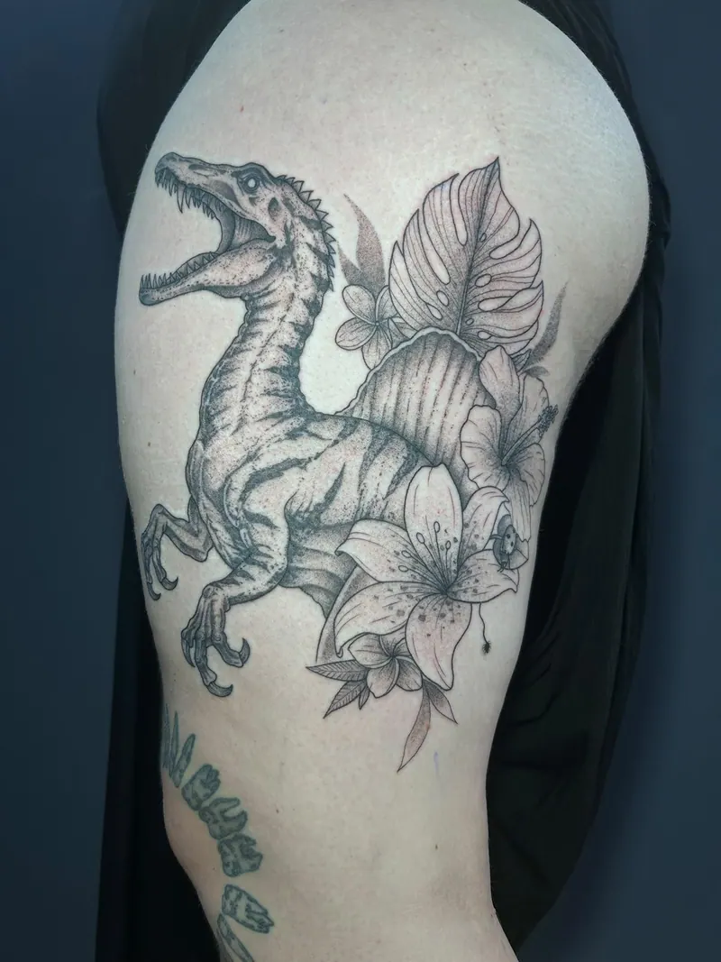 Black-&-Grey-Tattoo eines Raptors mit Lilien und Monstera-Blatt am Oberarm, gestochen von Cindy