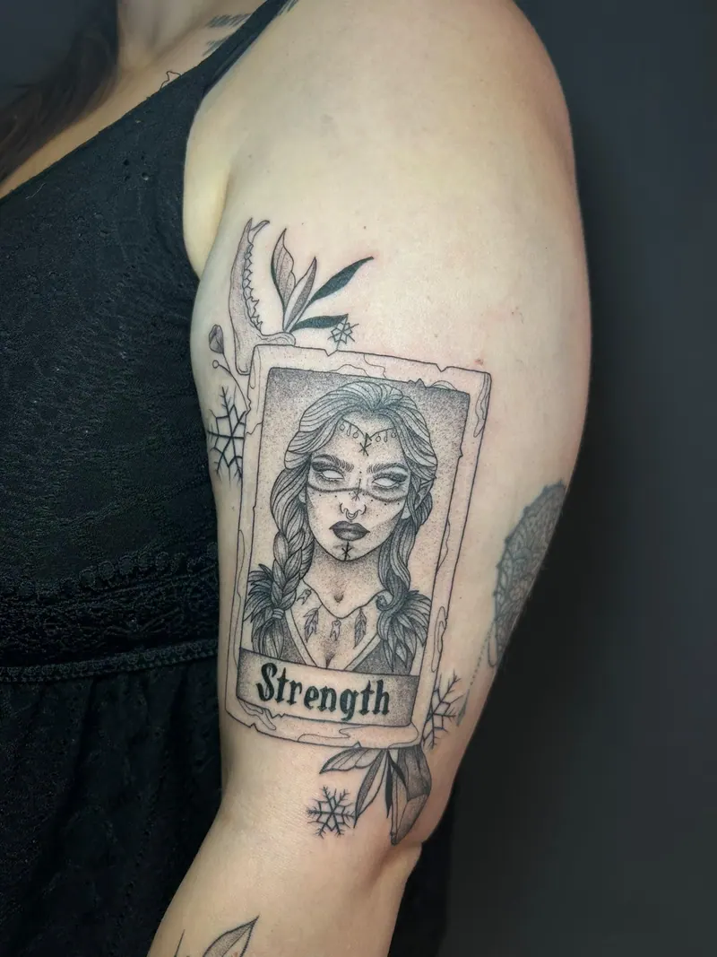 Tattoo einer Tarotkarte „Strength“ mit Frauenportrait, Blättern und Schneeflocken am Oberarm, gestochen von Cindy