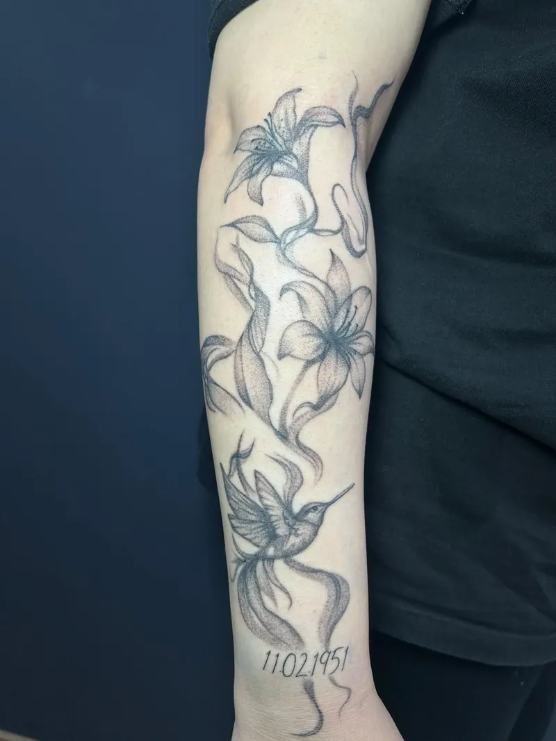 Tattoo von Lilien mit Kolibri und Datum am Unterarm, gestochen von Cindy