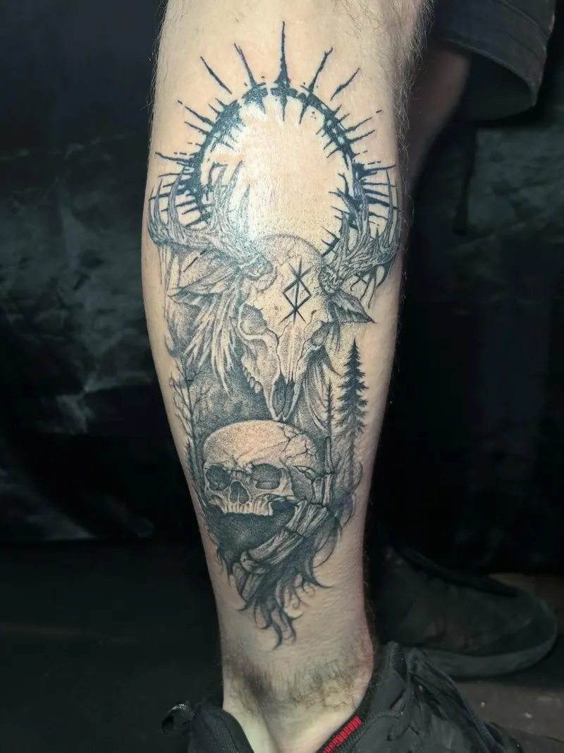 Black-&-Grey-Tattoo eines Hirschschädels mit Rune, Totenkopf und Tannen unter einem Strahlenkranz am Unterschenkel, gestochen von Cindy