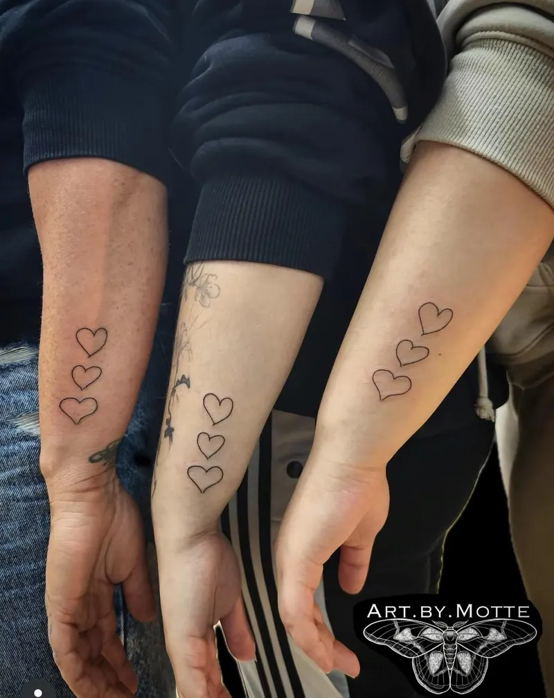 Fineline-Partner-Tattoo: jeweils drei Herzen an den Unterarmen dreier Personen, gestochen von Motte