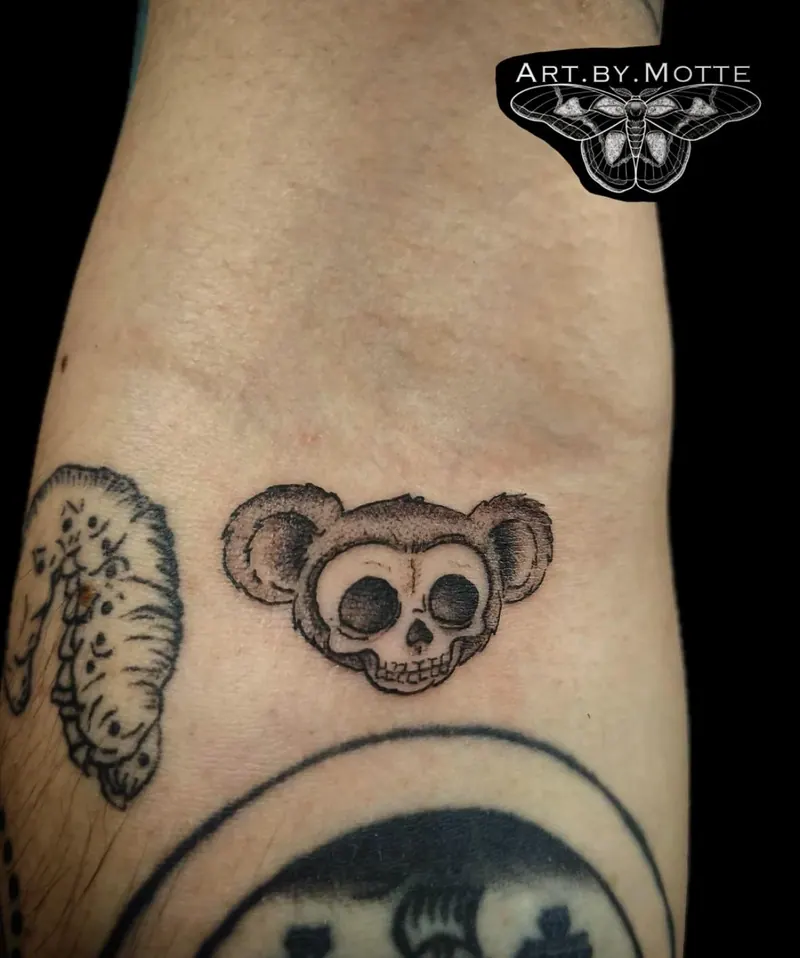 Blackwork-Tattoo eines Totenkopfs mit runden Mäuseohren am Arm, gestochen von Motte