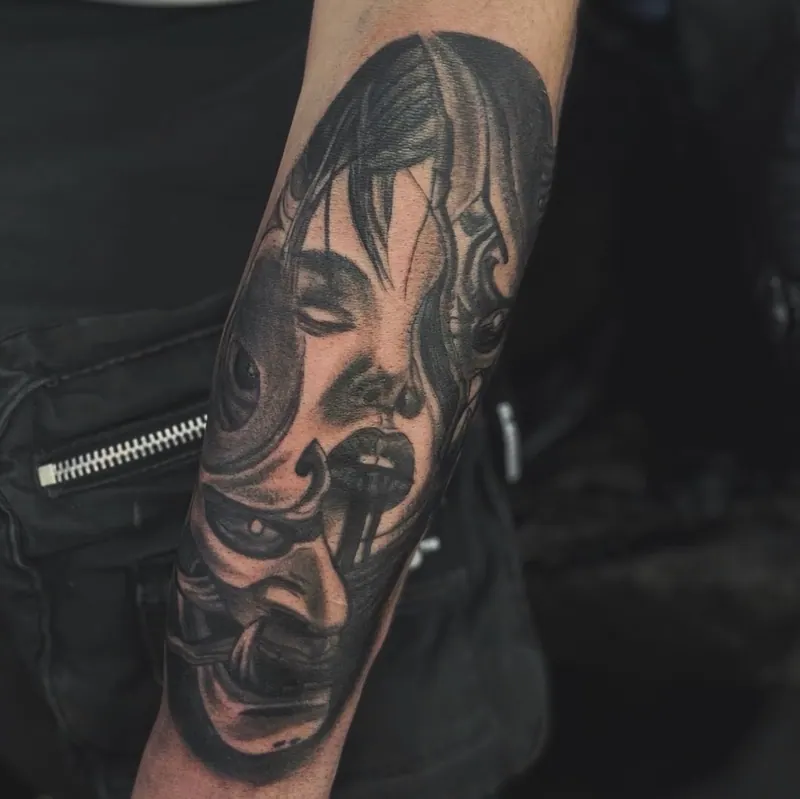 Black-&-Grey-Tattoo eines Frauengesichts mit dämonischer Maske am Unterarm, gestochen von Paul