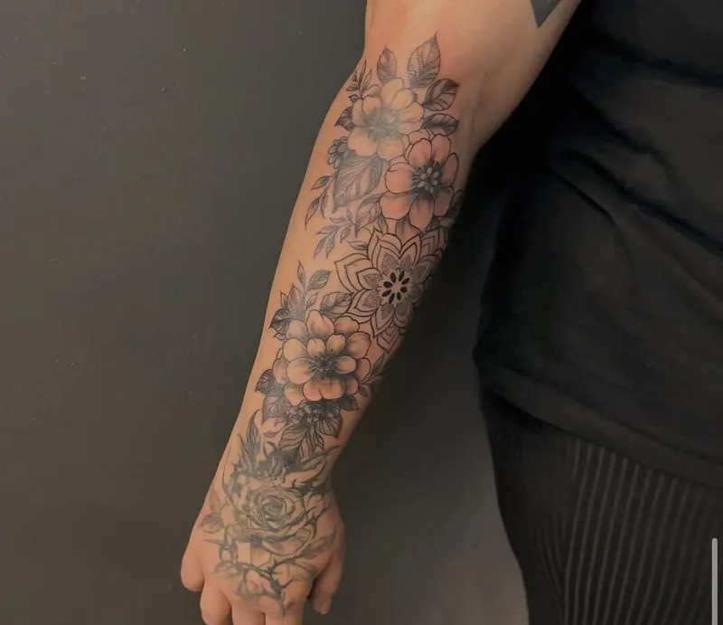 Black-&-Grey-Tattoo von Blüten mit kleinem Mandala an Unterarm und Hand, gestochen von Paul