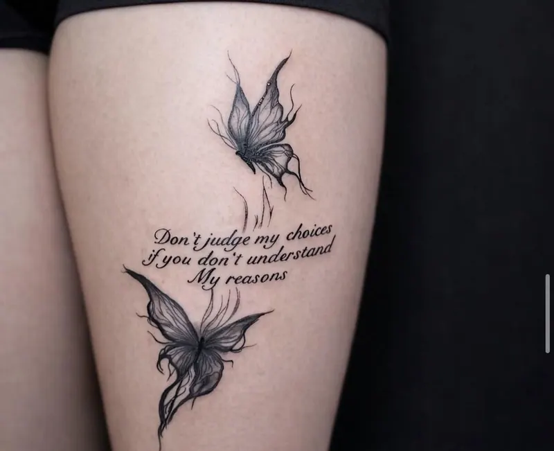 Tattoo zweier Schmetterlinge mit Schriftzug „Don’t judge my choices if you don’t understand my reasons“ am Oberschenkel, gestochen von Paul